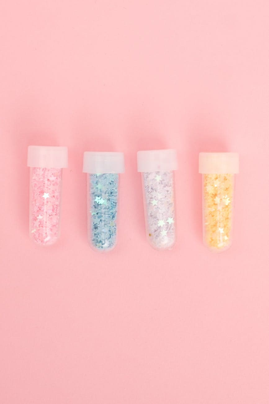 Four glitter-filled tubes arranged on a soft pink background for a vibrant festive effect.