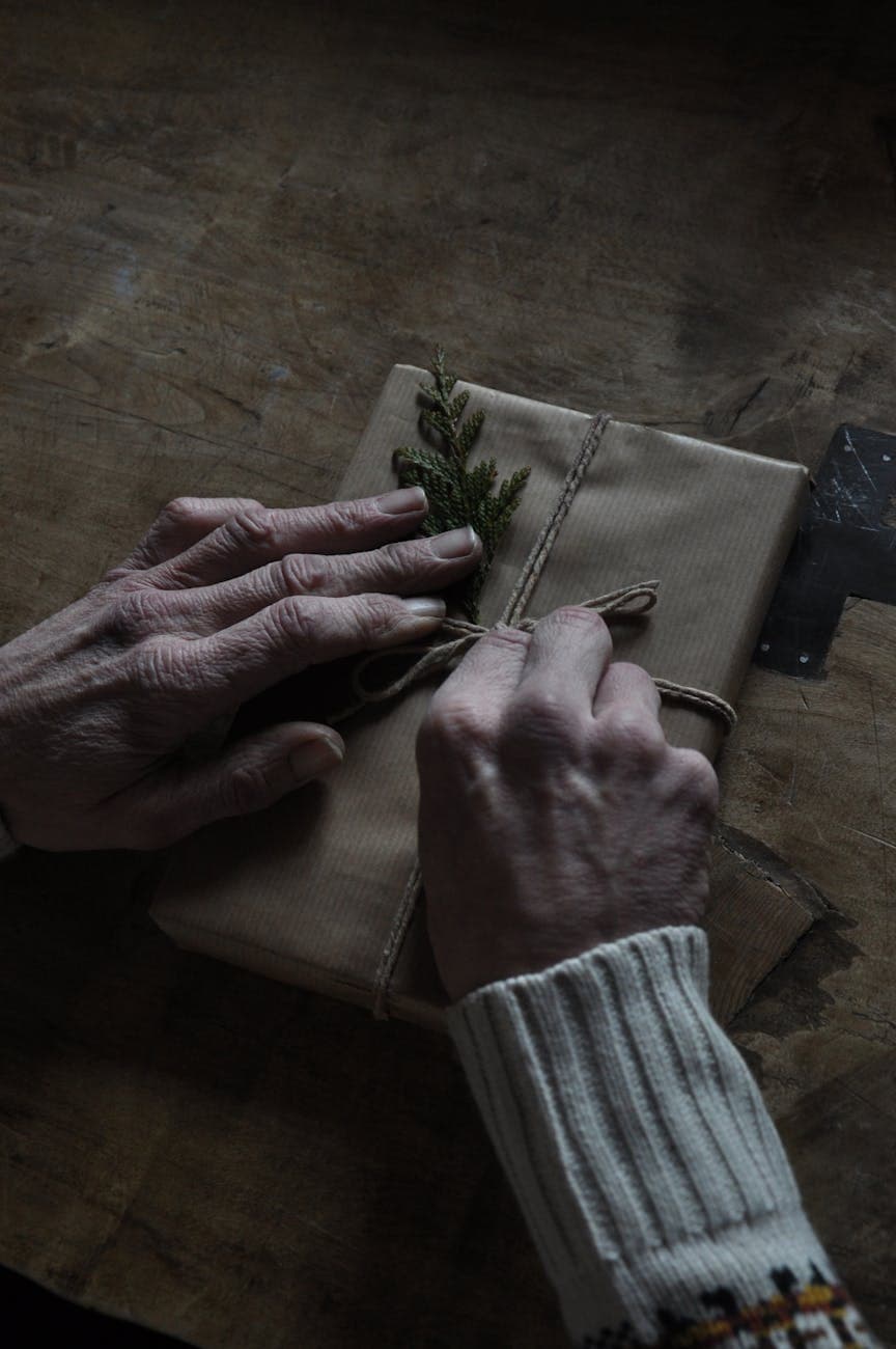 A pair of elderly hands tying twine around a rustic, handmade gift with natural decor.