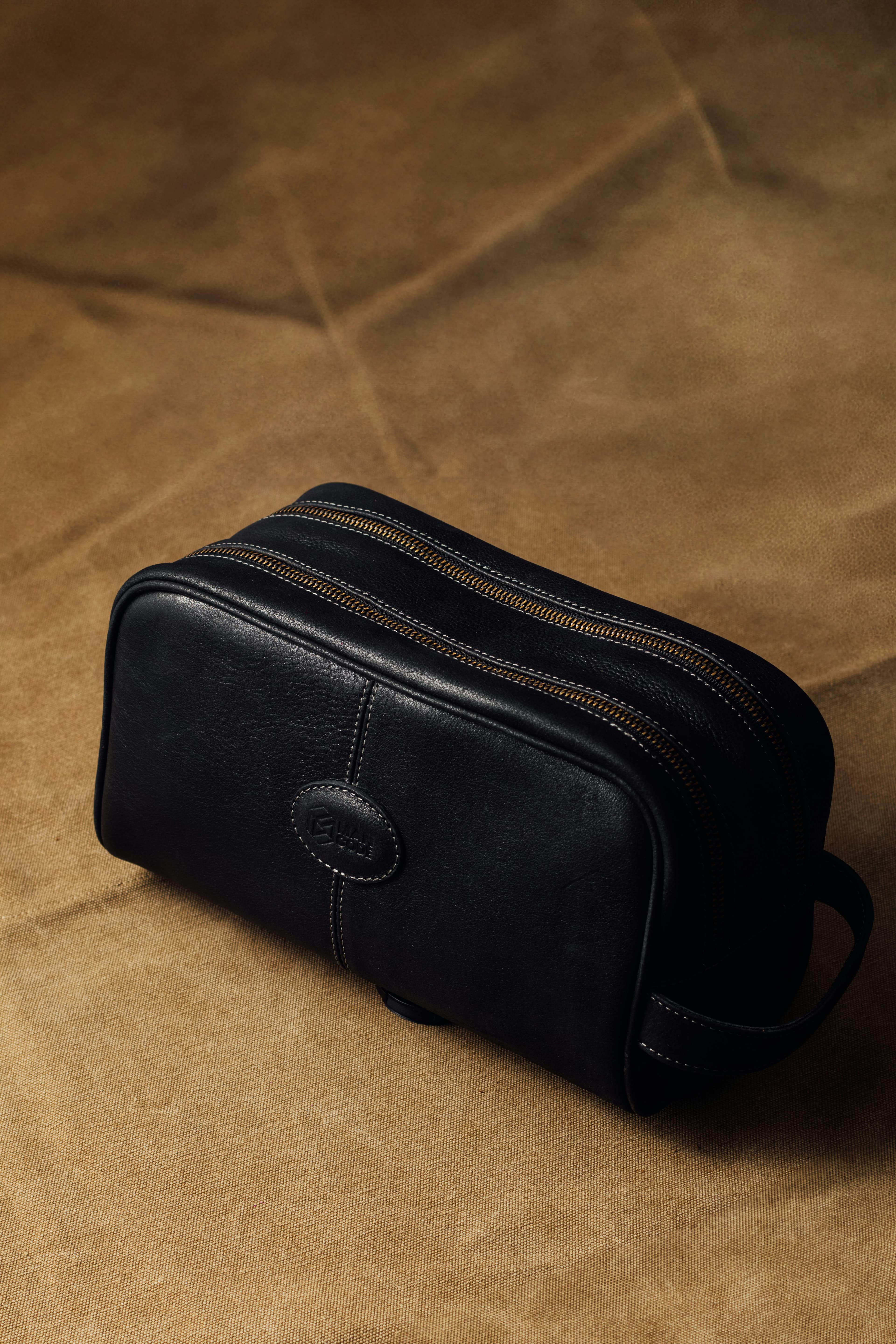 Sophisticated black leather dopp kit with dual zippers on a brown textured surface. Perfect for travel.
